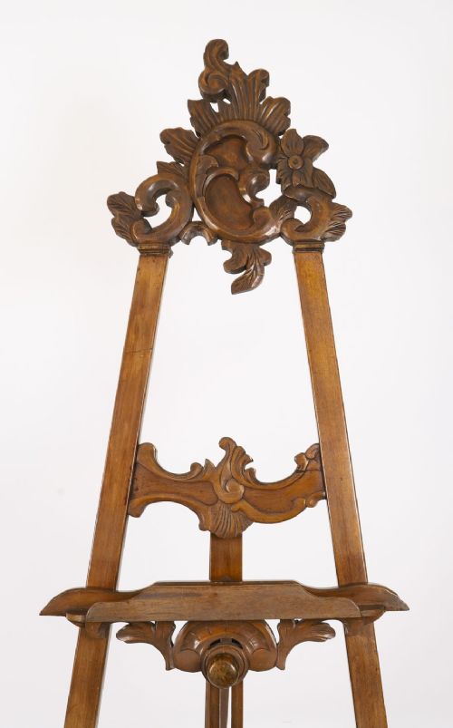 A 19th-century carved walnut artist easel featuring an ornate Rococo Revival scrollwork crest and an adjustable ledge on a tripod frame. View V