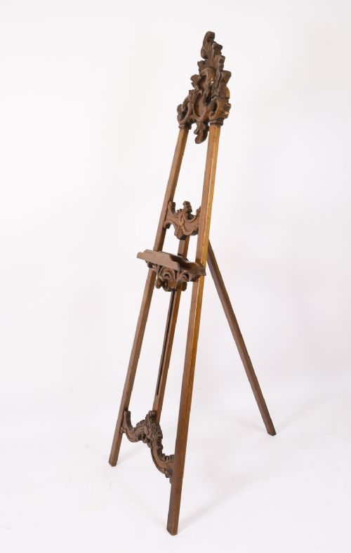 A 19th-century carved walnut artist easel featuring an ornate Rococo Revival scrollwork crest and an adjustable ledge on a tripod frame. View XII
