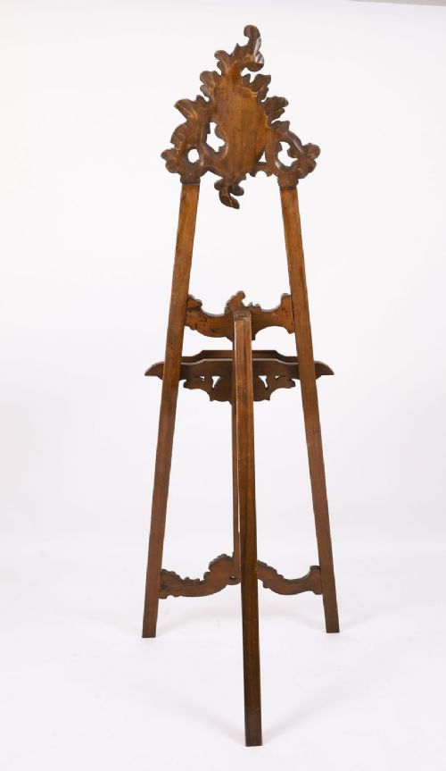 A 19th-century carved walnut artist easel featuring an ornate Rococo Revival scrollwork crest and an adjustable ledge on a tripod frame. View XIV