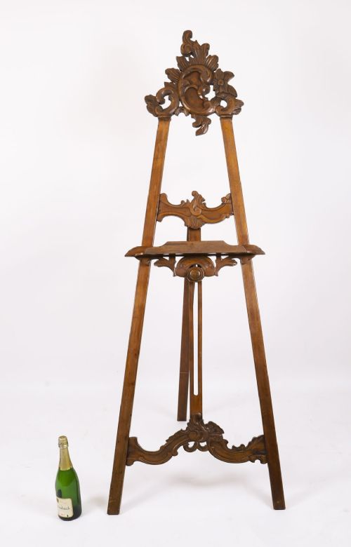 A 19th-century carved walnut artist easel featuring an ornate Rococo Revival scrollwork crest and an adjustable ledge on a tripod frame. View XV