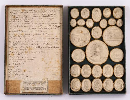 fig 1. An 18th-century set of cream plaster intaglio medallions arranged in a fitted green tray beside a handwritten manuscript index lid.