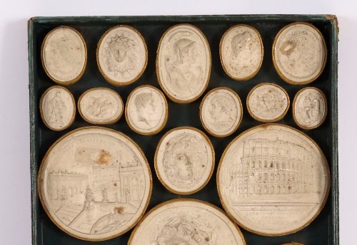 fig 3. An 18th-century set of cream plaster intaglio medallions arranged in a fitted green tray beside a handwritten manuscript index lid.