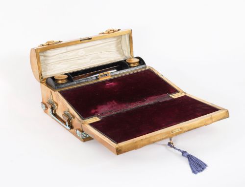 fig 1. A Victorian gilt brass and turquoise champleve enamel writing slope featuring a domed upper compartment, a sloped front lid, and a key with a purple tassel in the lock.
