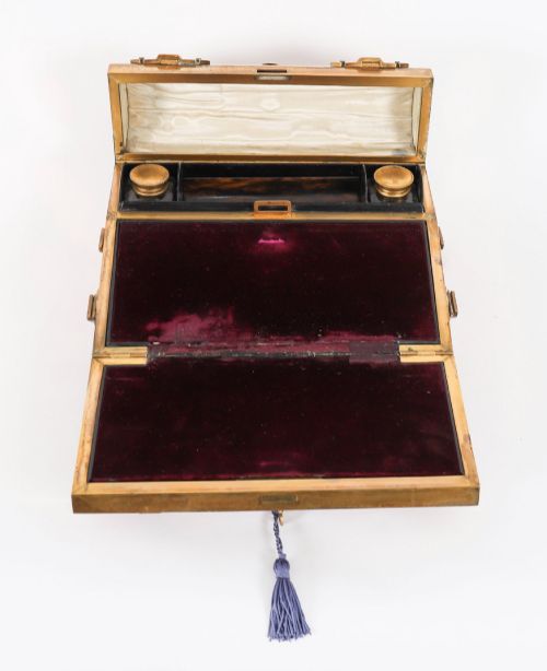 fig 7. A Victorian gilt brass and turquoise champleve enamel writing slope featuring a domed upper compartment, a sloped front lid, and a key with a purple tassel in the lock.