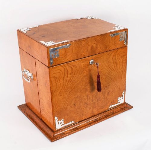 fig 3. A 19th-century Victorian figured oak three-bottle tantalus open to reveal three cut glass decanters, a fitted cribbage board, and a drop-front drawer containing a silver-plated tray and playing cards.