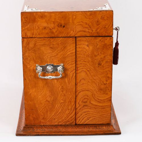 fig 10. A 19th-century Victorian figured oak three-bottle tantalus open to reveal three cut glass decanters, a fitted cribbage board, and a drop-front drawer containing a silver-plated tray and playing cards.