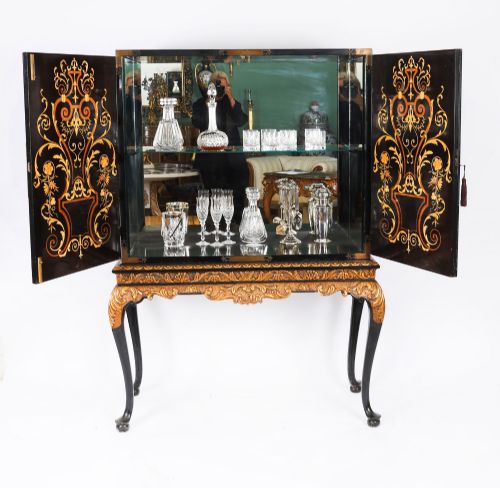 fig 1. A black lacquered and inlaid wooden cocktail cabinet featuring ornate floral marquetry and decorative brass straps, resting on a carved gilded stand with cabriole legs.