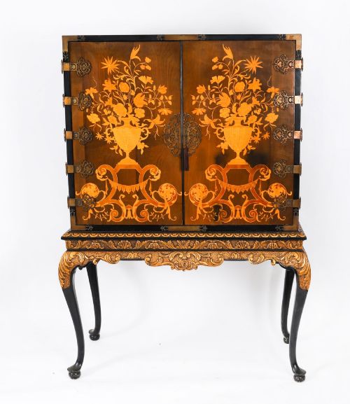 fig 2. A black lacquered and inlaid wooden cocktail cabinet featuring ornate floral marquetry and decorative brass straps, resting on a carved gilded stand with cabriole legs.