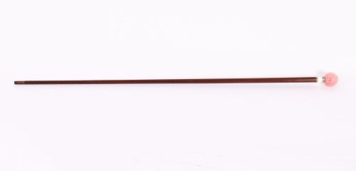 fig 1. An antique walking stick featuring a spherical pink quartz pommel set above a white enamel collar with silver beaded borders and a dark wood shaft.