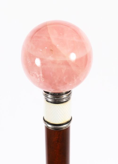 fig 2. An antique walking stick featuring a spherical pink quartz pommel set above a white enamel collar with silver beaded borders and a dark wood shaft.