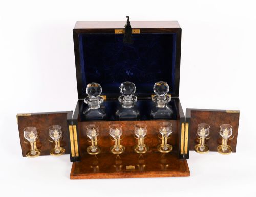 fig 2. An open and closed 19th-century Victorian burr walnut tantalus box containing three cut crystal decanters, brass-mounted liqueur glasses, and a deep blue velvet lining.