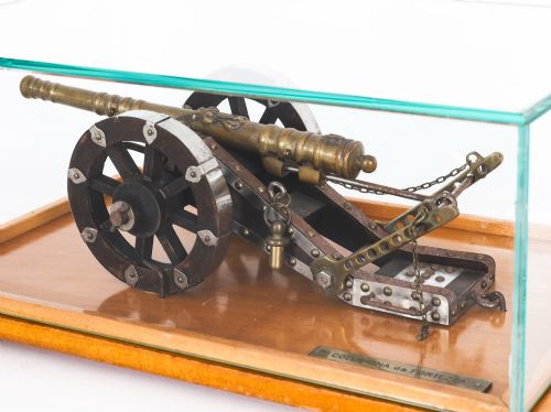 fig 2. A 19th-century bronze model cannon mounted on a dark wooden carriage and enclosed within a clear glass display case.