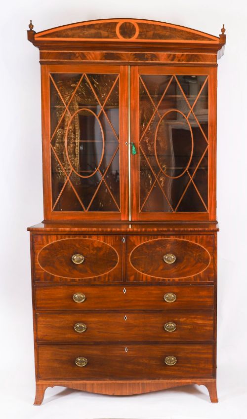fig 1. An antique George III flame mahogany secretaire bookcase featuring a shaped pediment, two upper astragal glazed doors, and a lower four-drawer chest base with brass ring handles.