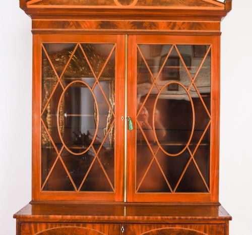 fig 4. An antique George III flame mahogany secretaire bookcase featuring a shaped pediment, two upper astragal glazed doors, and a lower four-drawer chest base with brass ring handles.