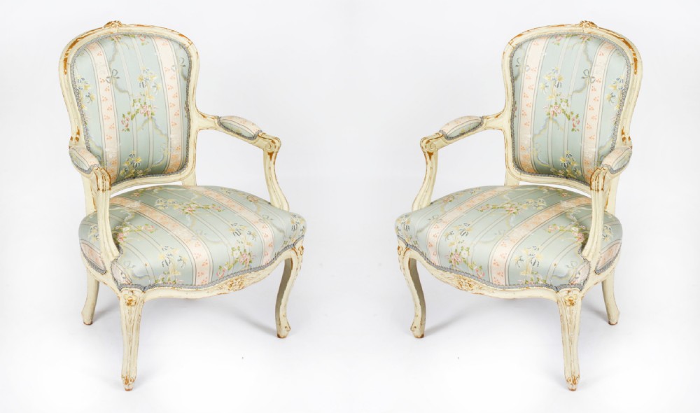 A pair of 19th-century French Louis Revival armchairs featuring distressed cream-painted carved wooden frames and striped pastel floral silk upholstery. View XVIII