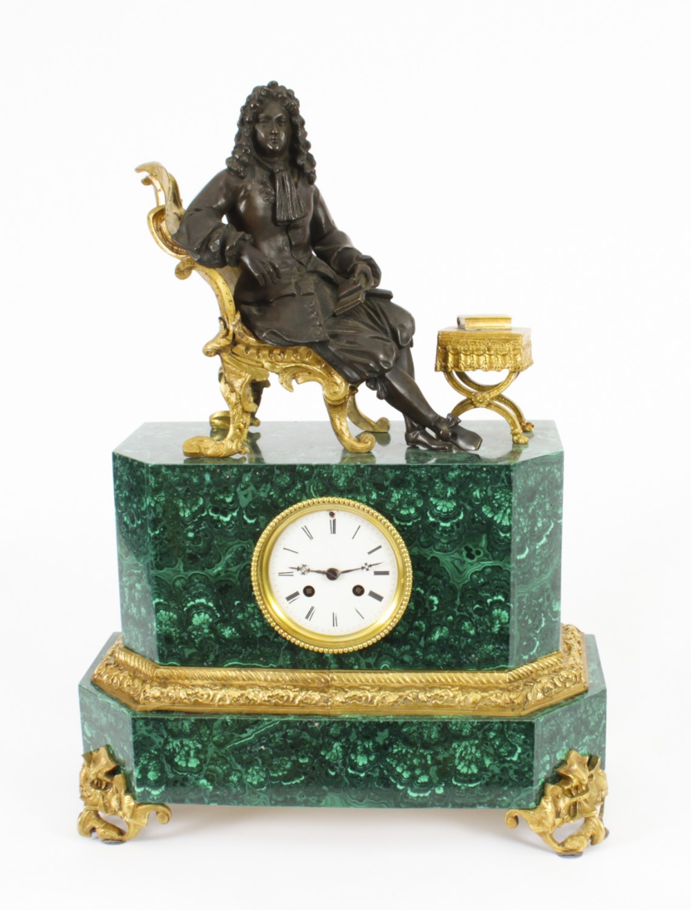 A nineteenth-century French mantel clock featuring a green malachite base with gilt bronze mounts, a white enamel dial with Roman numerals, and a dark bronze figure seated on a gilt chair.