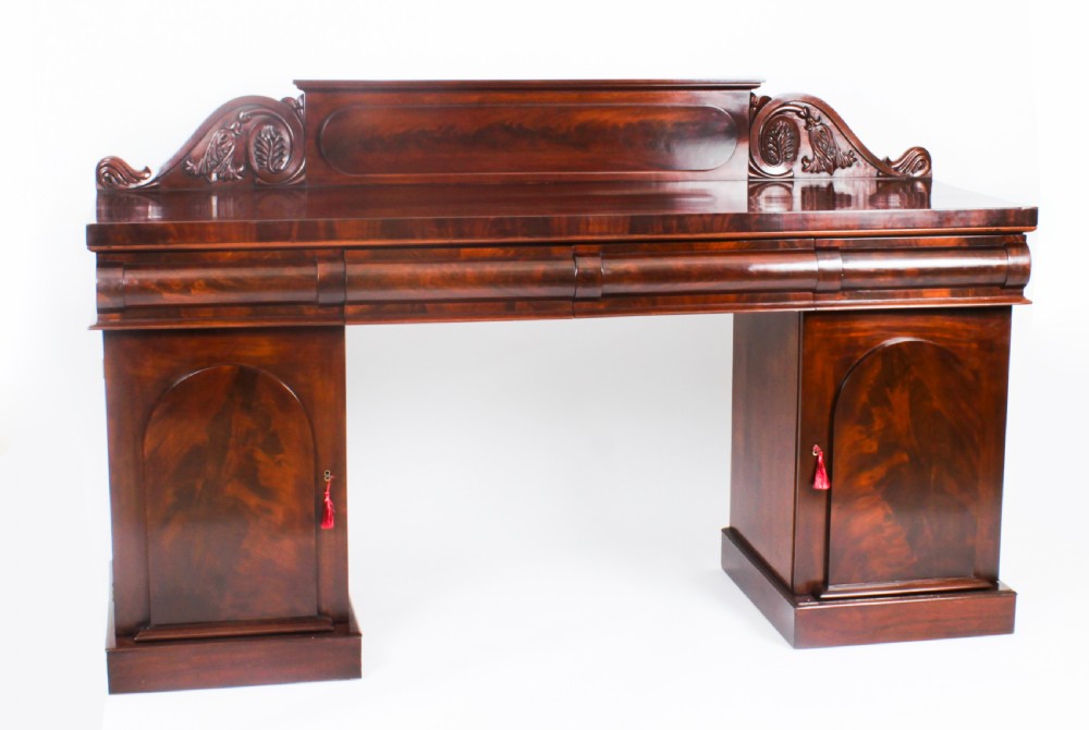 A mid-nineteenth-century flame mahogany pedestal sideboard featuring twin cupboard doors with arched panels and a carved scroll splashback.