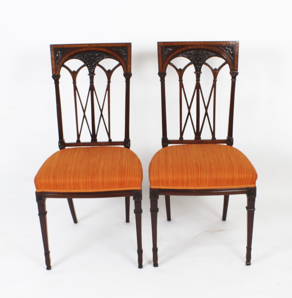 A pair of antique Sheraton Revival mahogany side chairs featuring carved arched back tracery, turned front legs, and orange striped fabric seats.