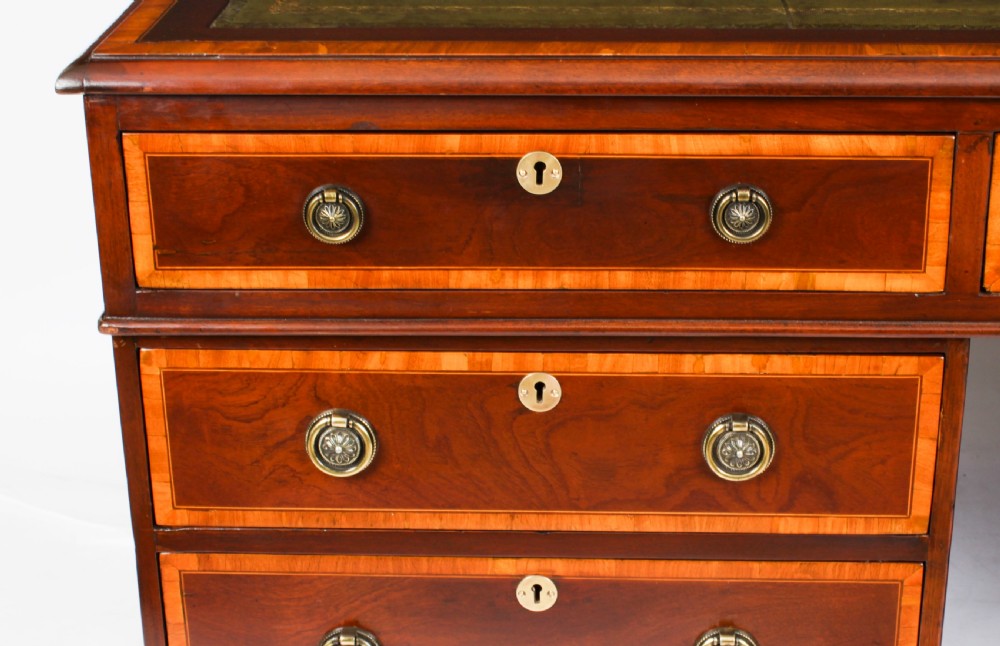 A Victorian flame mahogany partners pedestal desk featuring a green leather inset top and crossbanded drawer fronts with brass ring handles. View XII
