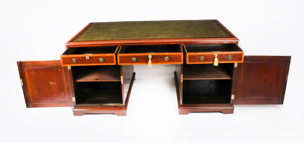 A Victorian flame mahogany partners pedestal desk featuring a green leather inset top and crossbanded drawer fronts with brass ring handles. View XIX