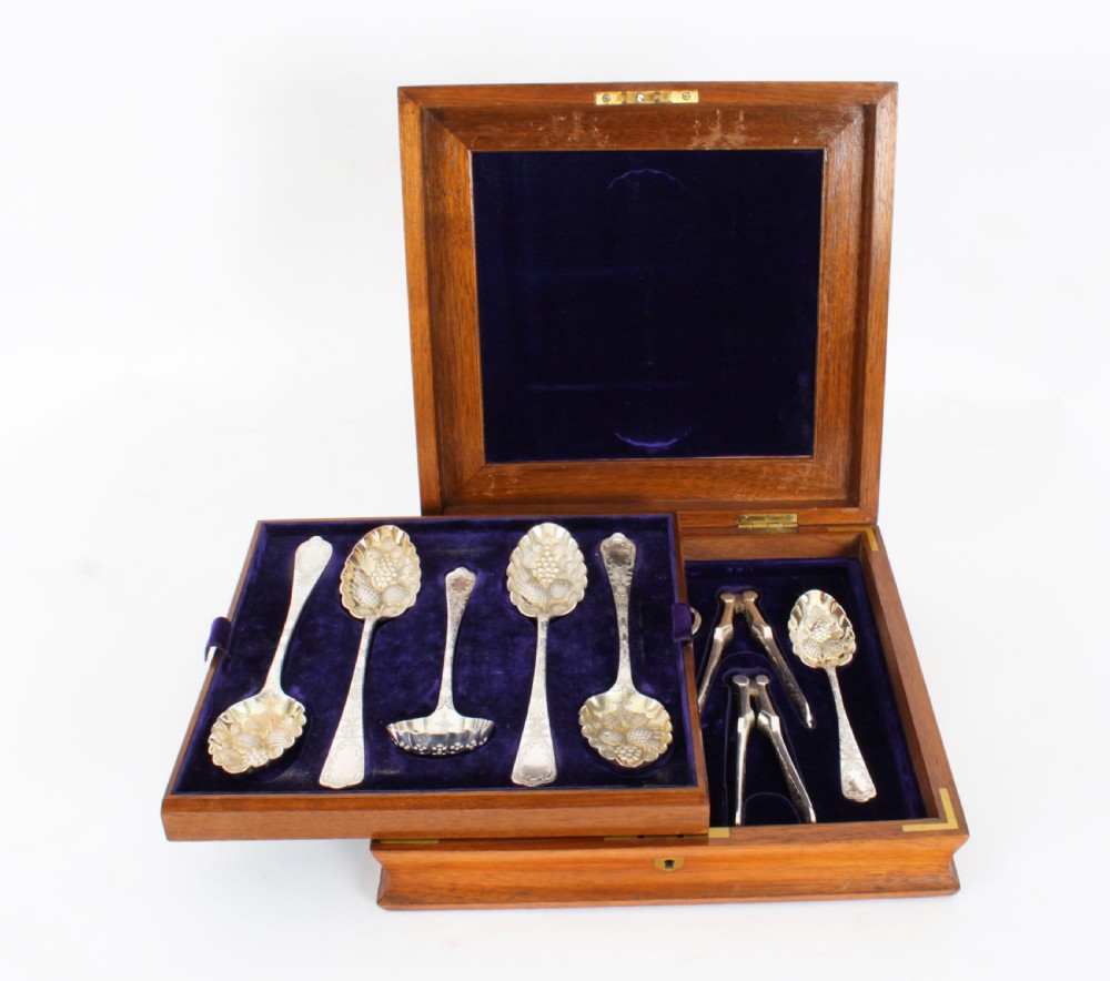 An open wooden case lined with deep purple velvet containing a silver-plated fruit serving set with embossed spoons and nutcrackers.