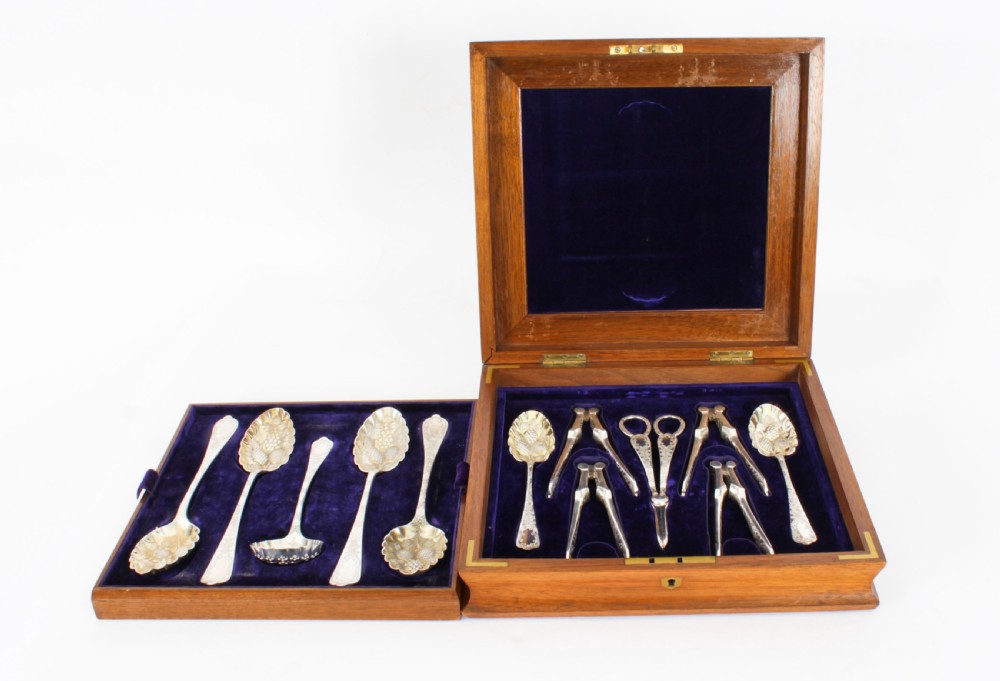 An open wooden case lined with deep purple velvet containing a silver-plated fruit serving set with embossed spoons and nutcrackers. View II