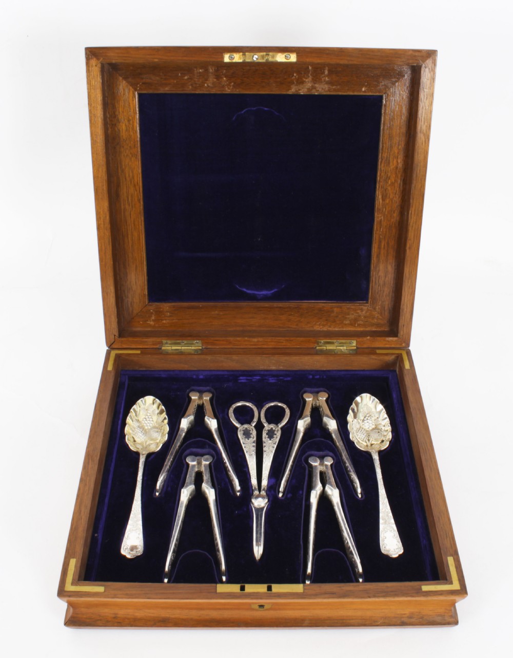 An open wooden case lined with deep purple velvet containing a silver-plated fruit serving set with embossed spoons and nutcrackers. View III