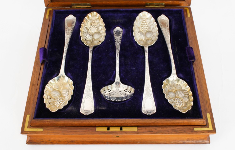 An open wooden case lined with deep purple velvet containing a silver-plated fruit serving set with embossed spoons and nutcrackers. View V