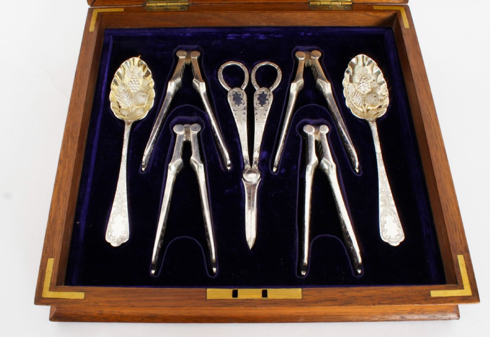 An open wooden case lined with deep purple velvet containing a silver-plated fruit serving set with embossed spoons and nutcrackers. View VI