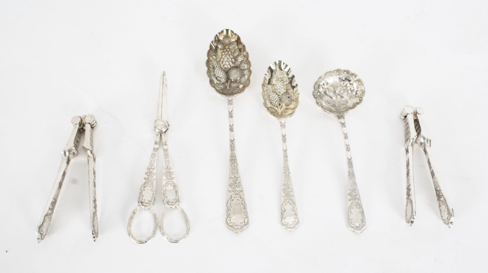 An open wooden case lined with deep purple velvet containing a silver-plated fruit serving set with embossed spoons and nutcrackers. View VII