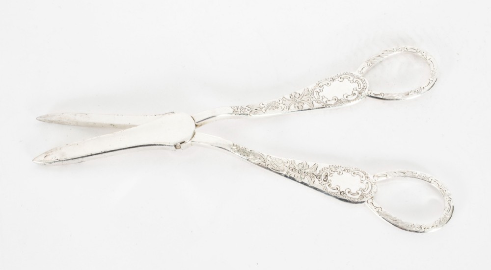 An open wooden case lined with deep purple velvet containing a silver-plated fruit serving set with embossed spoons and nutcrackers. View XXV