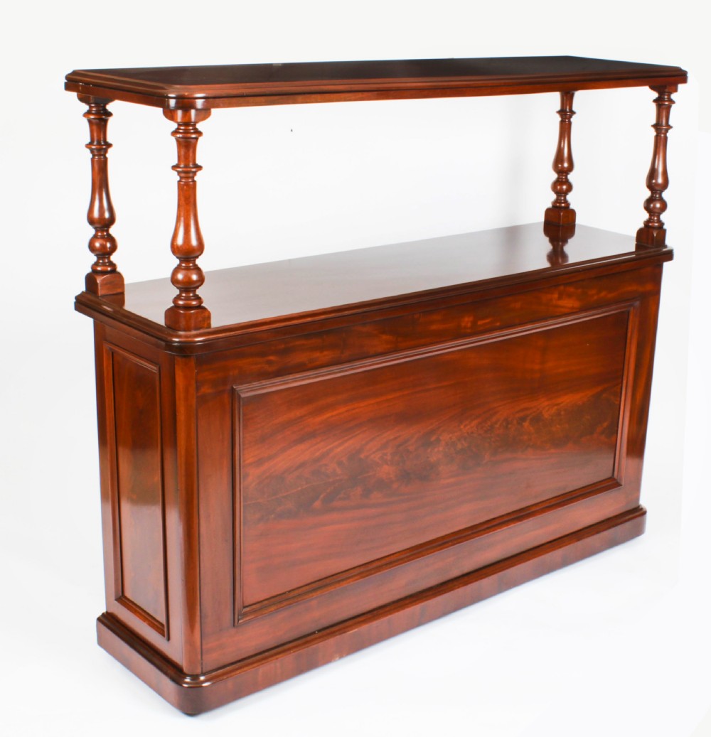 A Victorian flame mahogany dry bar featuring an elevated upper shelf supported by four turned balusters over a panelled lower counter.
