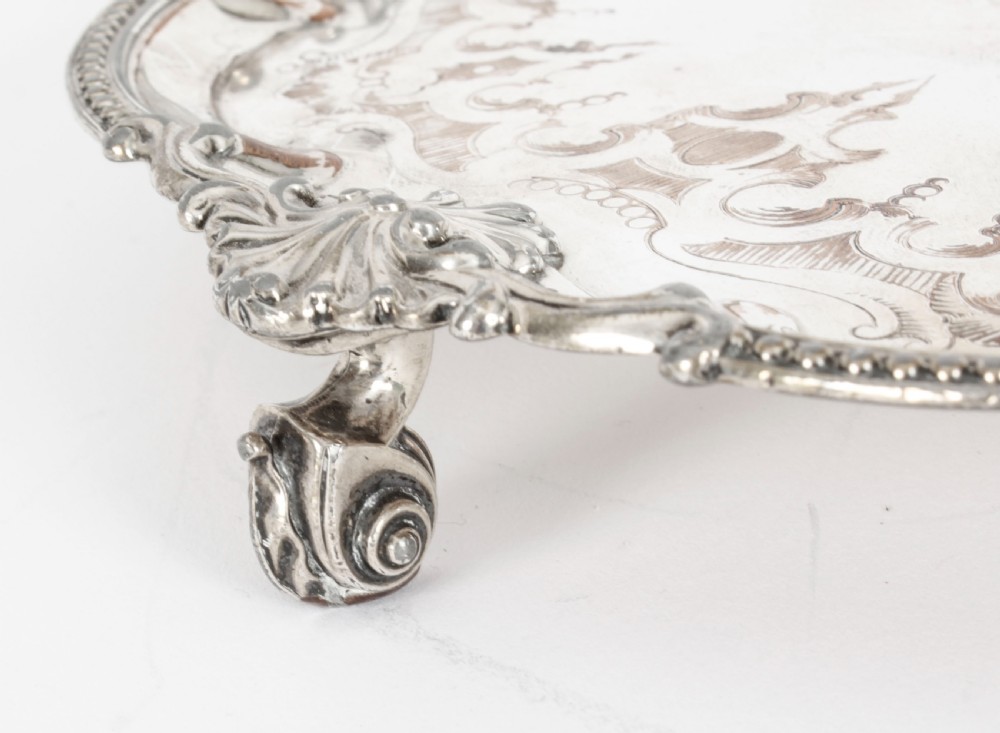A Georgian Old Sheffield plate silver-plated salver featuring chased scroll engravings, shell motifs on a beaded rim, and resting on short feet. View V