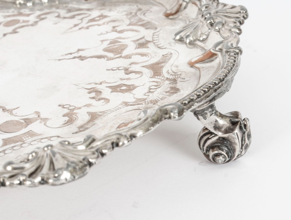 A Georgian Old Sheffield plate silver-plated salver featuring chased scroll engravings, shell motifs on a beaded rim, and resting on short feet. View VI