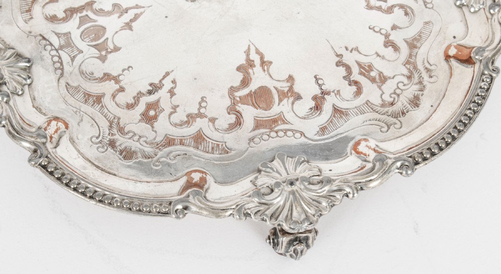 A Georgian Old Sheffield plate silver-plated salver featuring chased scroll engravings, shell motifs on a beaded rim, and resting on short feet. View VII