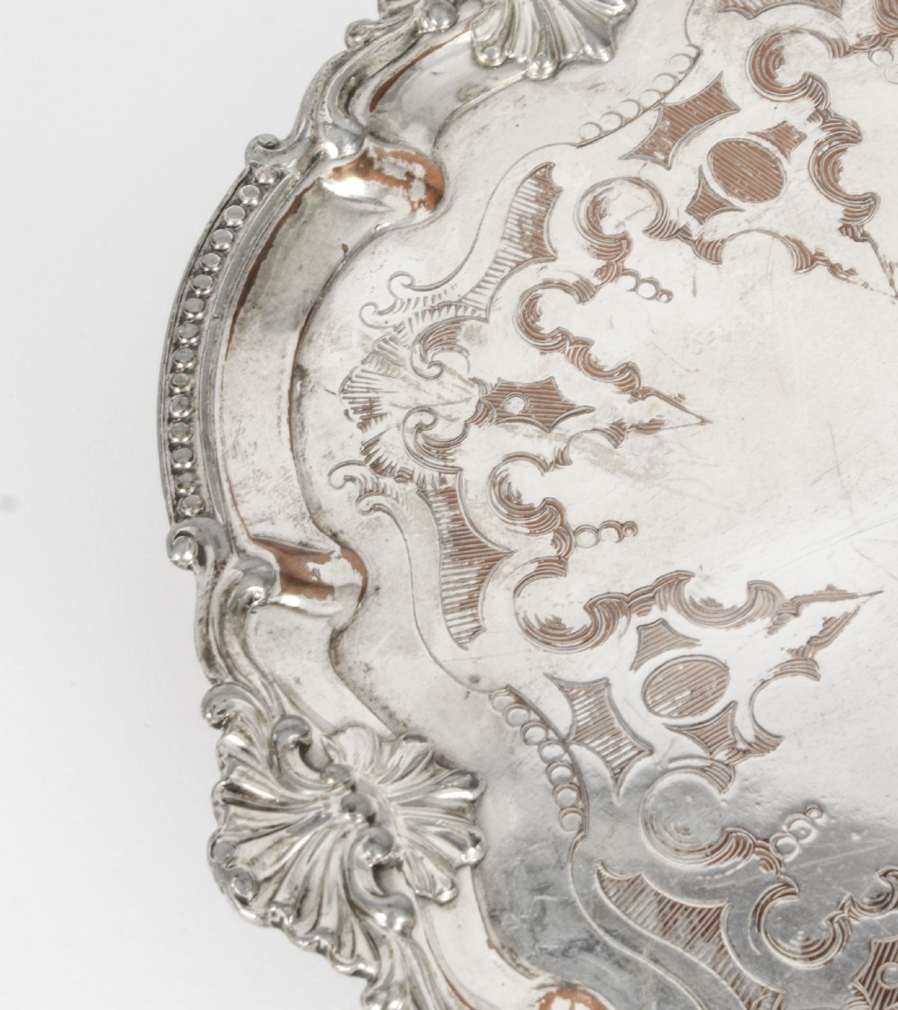 A Georgian Old Sheffield plate silver-plated salver featuring chased scroll engravings, shell motifs on a beaded rim, and resting on short feet. View VIII