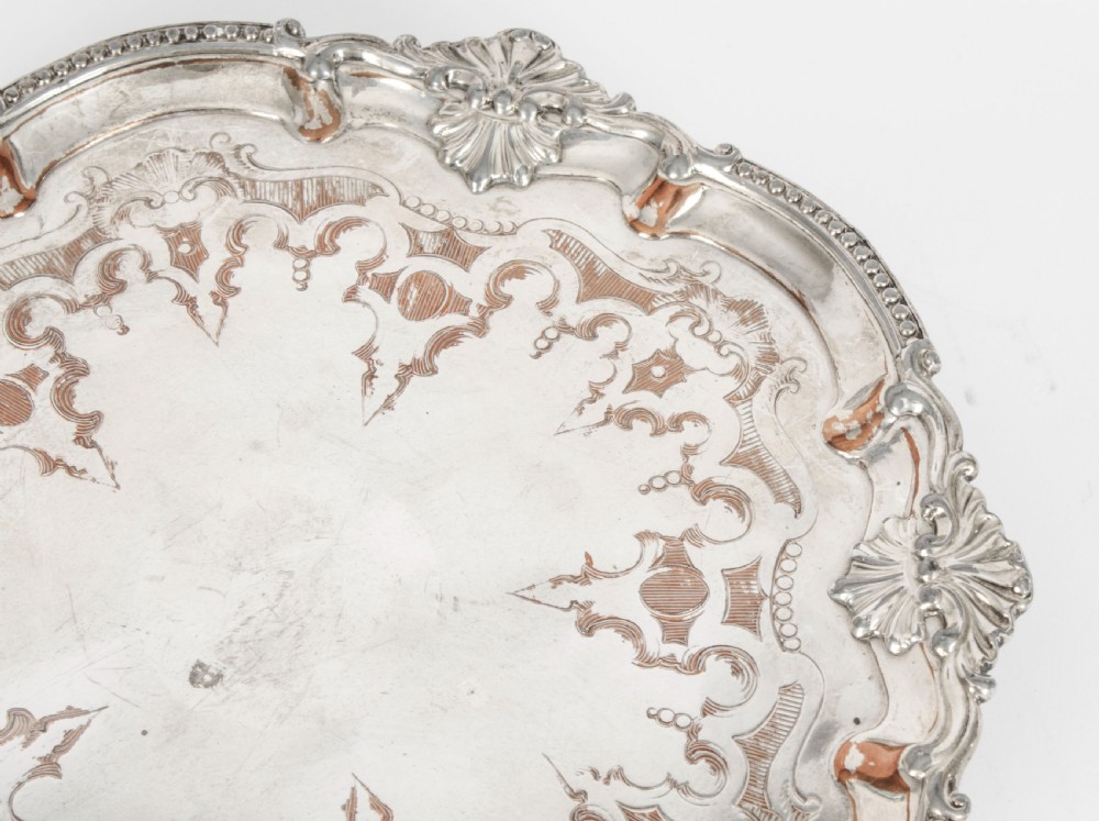 A Georgian Old Sheffield plate silver-plated salver featuring chased scroll engravings, shell motifs on a beaded rim, and resting on short feet. View IX