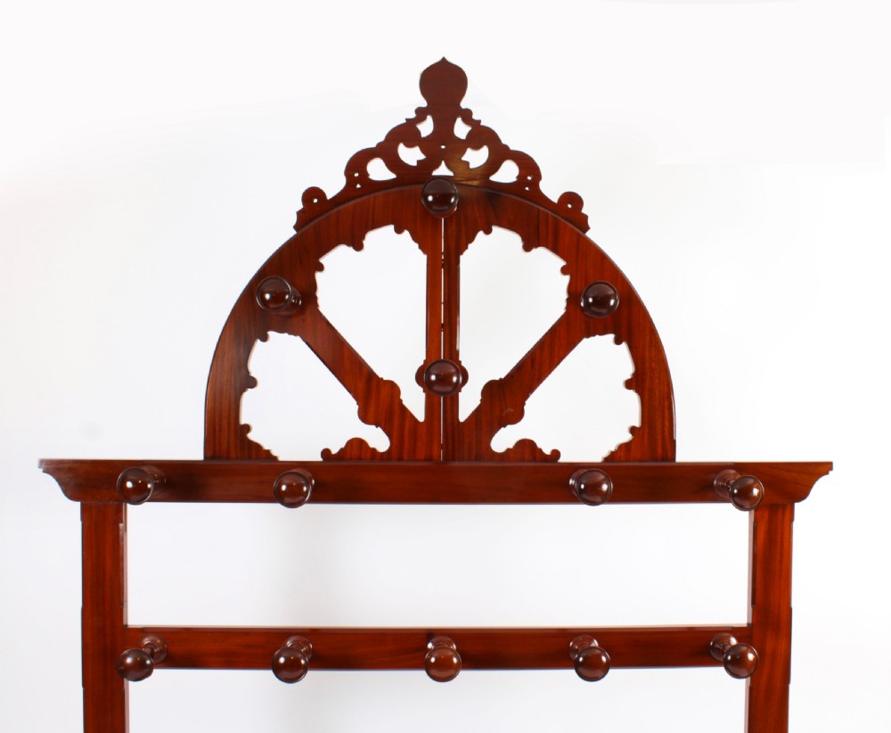 A Victorian mahogany hall stand featuring an arched fretwork top with wooden peg hooks, a brass umbrella bar, and a fitted drip pan base. View V
