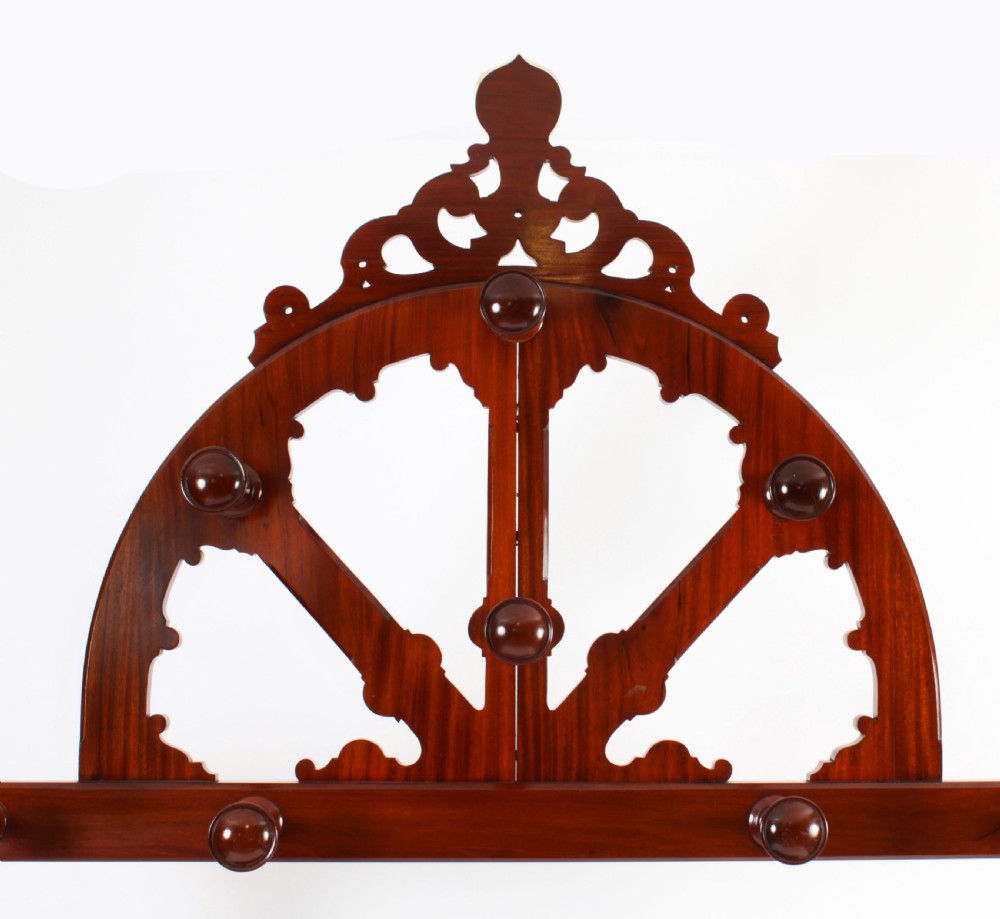 A Victorian mahogany hall stand featuring an arched fretwork top with wooden peg hooks, a brass umbrella bar, and a fitted drip pan base. View VI