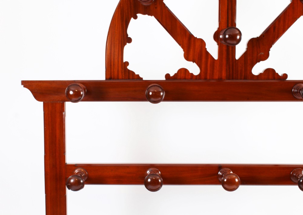 A Victorian mahogany hall stand featuring an arched fretwork top with wooden peg hooks, a brass umbrella bar, and a fitted drip pan base. View VIII