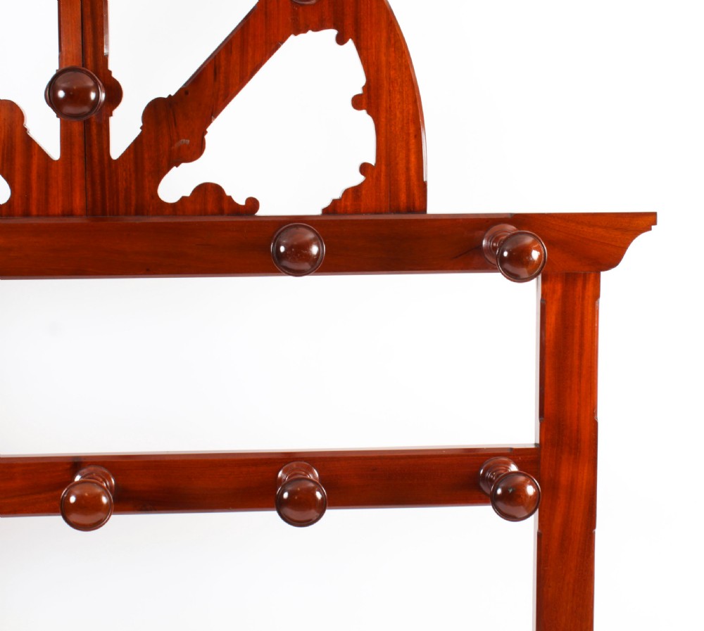 A Victorian mahogany hall stand featuring an arched fretwork top with wooden peg hooks, a brass umbrella bar, and a fitted drip pan base. View IX