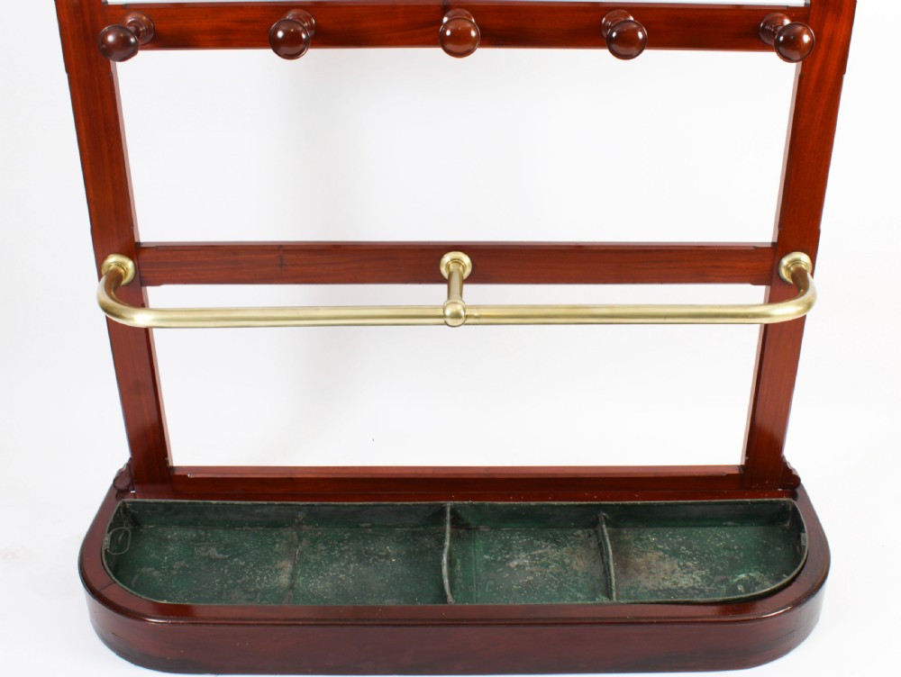 A Victorian mahogany hall stand featuring an arched fretwork top with wooden peg hooks, a brass umbrella bar, and a fitted drip pan base. View X