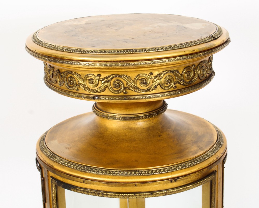 A 19th-century French giltwood cylindrical pedestal display cabinet featuring curved glass panels, an interior shelf, and carved guilloche mouldings. View IV