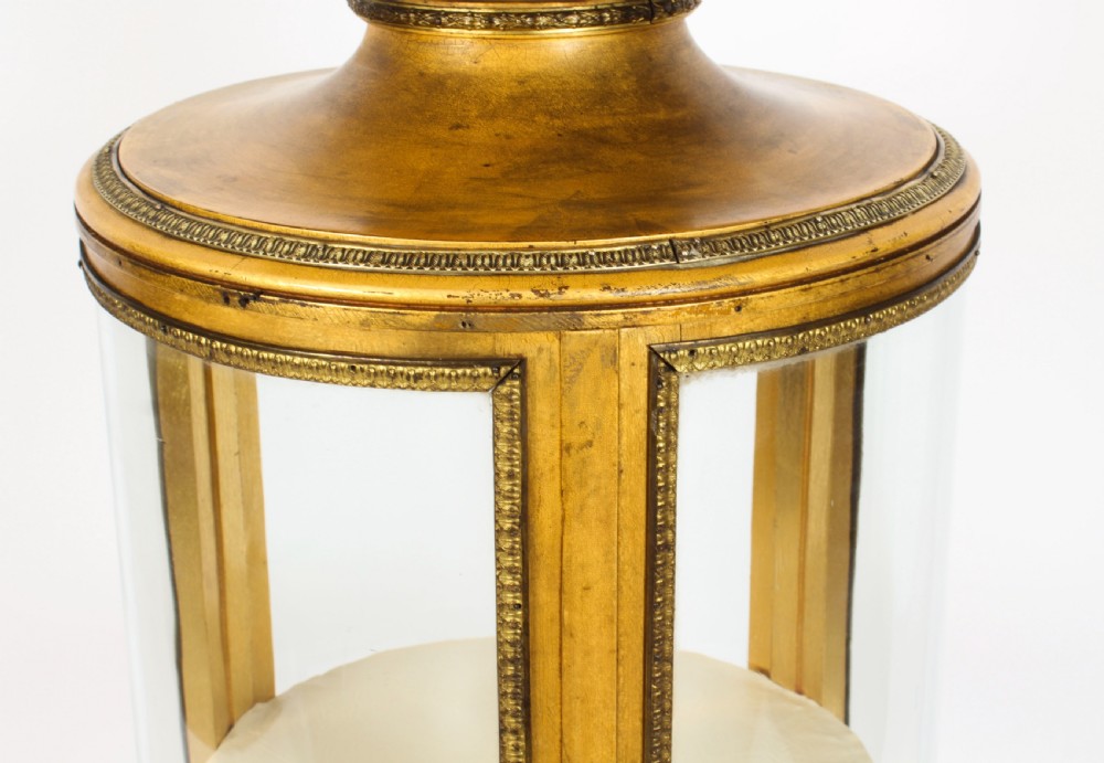 A 19th-century French giltwood cylindrical pedestal display cabinet featuring curved glass panels, an interior shelf, and carved guilloche mouldings. View VI