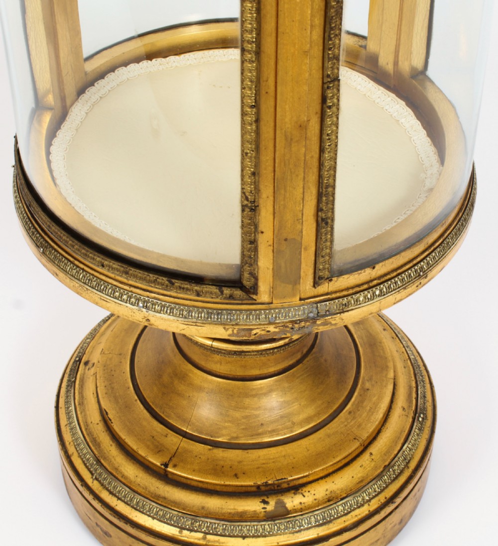 A 19th-century French giltwood cylindrical pedestal display cabinet featuring curved glass panels, an interior shelf, and carved guilloche mouldings. View IX