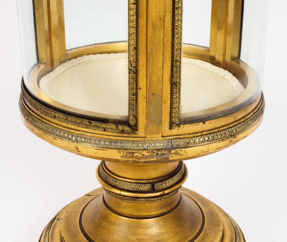 A 19th-century French giltwood cylindrical pedestal display cabinet featuring curved glass panels, an interior shelf, and carved guilloche mouldings. View X
