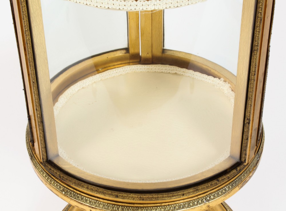 A 19th-century French giltwood cylindrical pedestal display cabinet featuring curved glass panels, an interior shelf, and carved guilloche mouldings. View XV