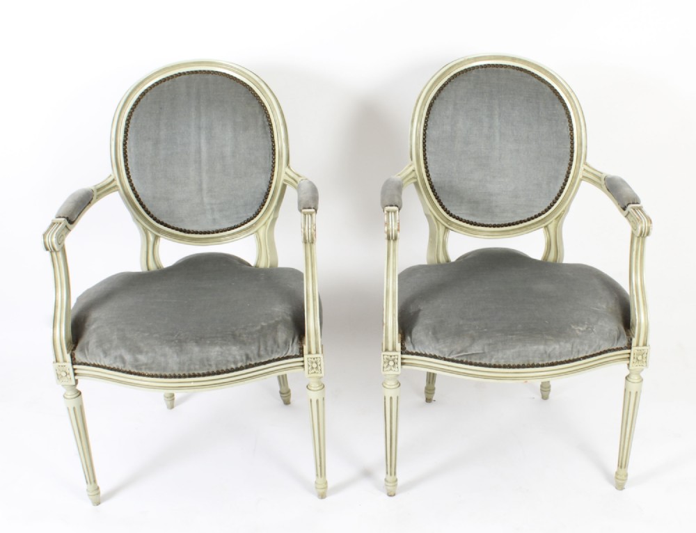 A pair of early 20th-century French Louis XVI Revival armchairs with off-white painted frames, oval backs, and grey velvet upholstery.