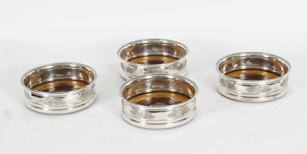 A set of four circular Regency period Old Sheffield Plate wine coasters with turned wooden bases and foliage chased silver rims.
