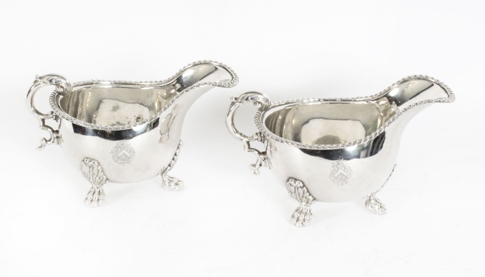 A pair of 19th-century silver-plated sauce boats featuring scroll handles, engraved crests, and claw feet against a white background.